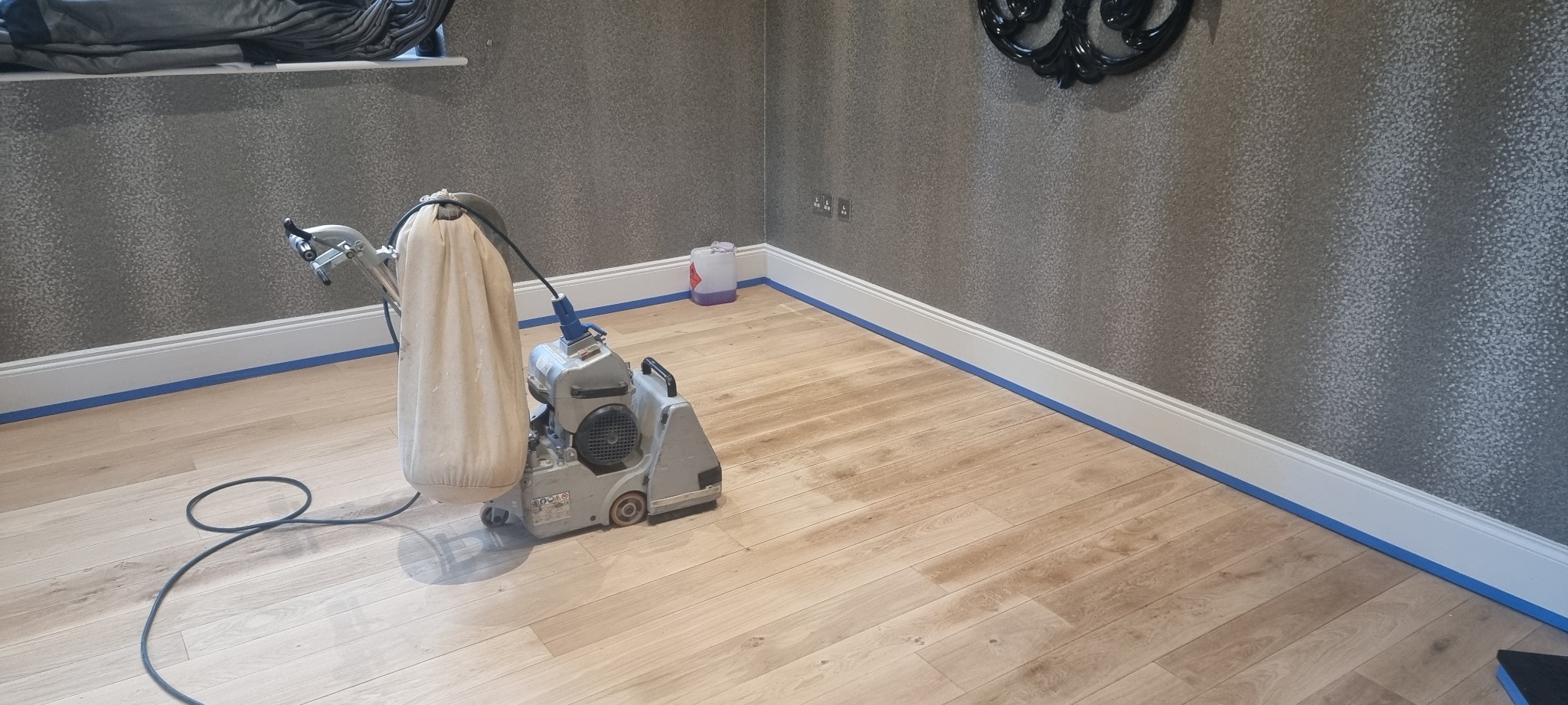 Professional drum sander positioned on partially sanded oak plank flooring inside a taped-off room—illustrating expert Wood Floor Sanding in Woking.