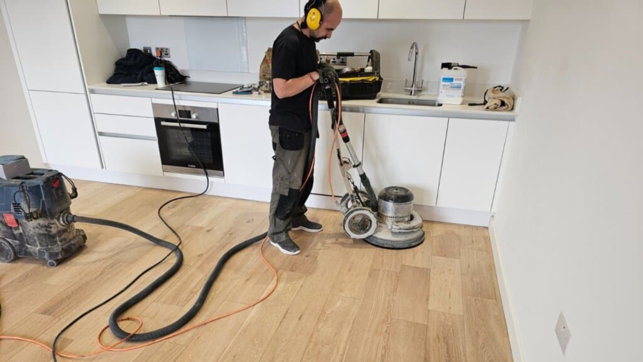 Dust-free sanding of a wide-plank oak kitchen floor by a technician wearing ear defenders—capturing expert Wood Floor Sanding in Woking.