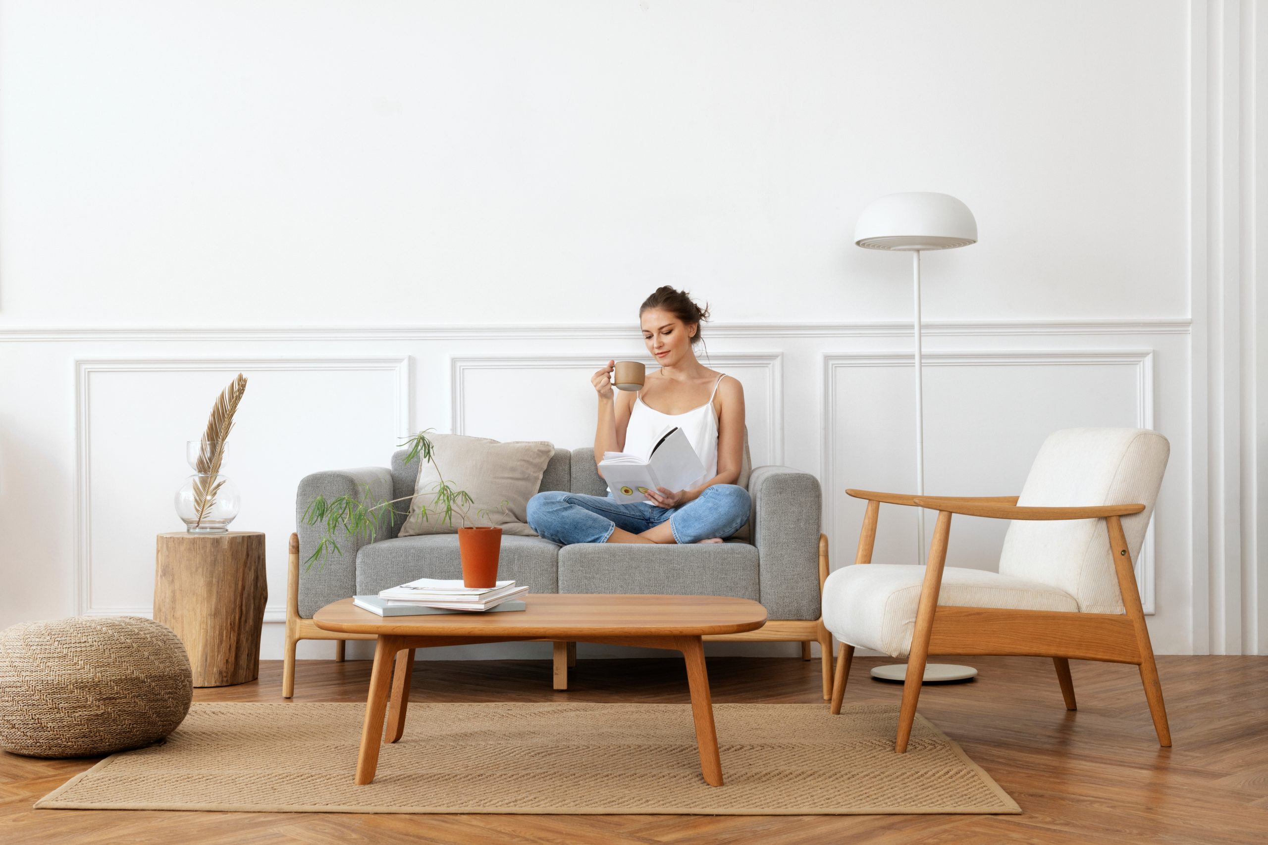 Woman relaxing with a book and coffee in a minimalist lounge featuring a freshly restored herringbone oak parquet floor—showcasing the results of Wood Floor Sanding in Woking.