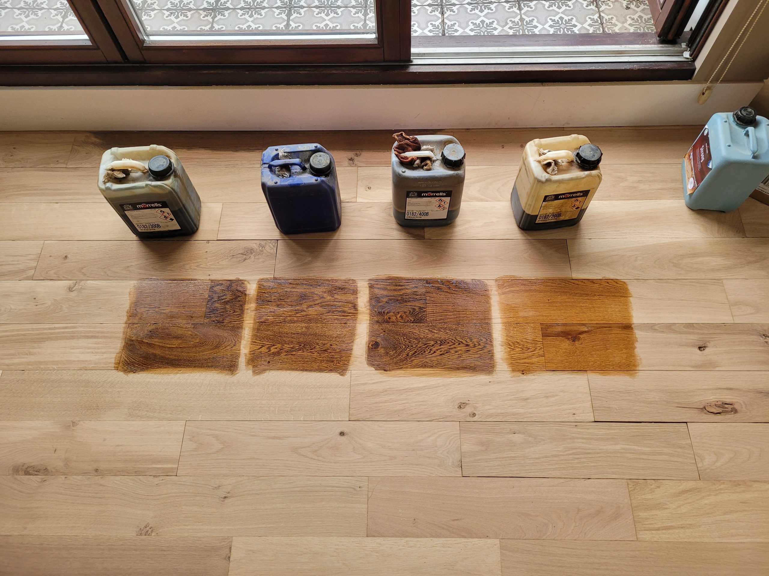 Furious Fixes in Woking: stain-test swatches on a European oak engineered plank floor to select the ideal colour before restoration.
