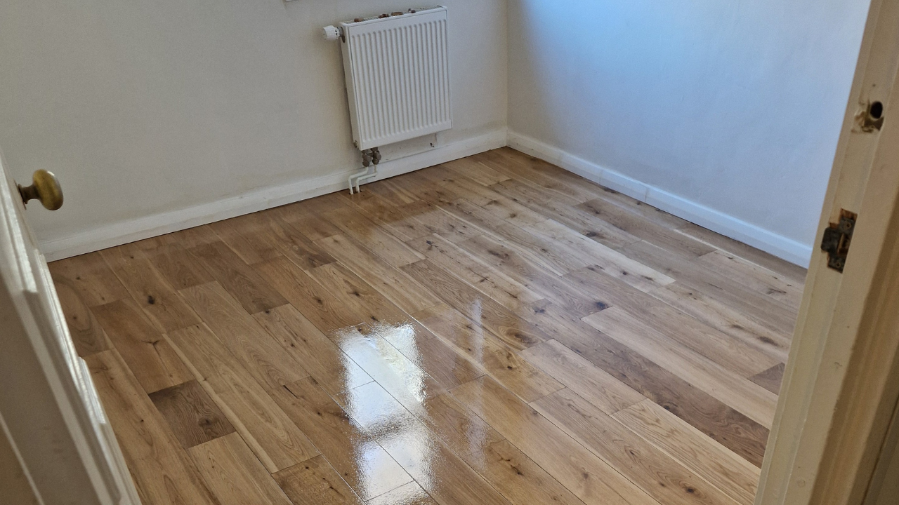 Furious Fixes in Woking: freshly finished European oak solid plank hardwood floor with a high-gloss sheen reflecting window light.
