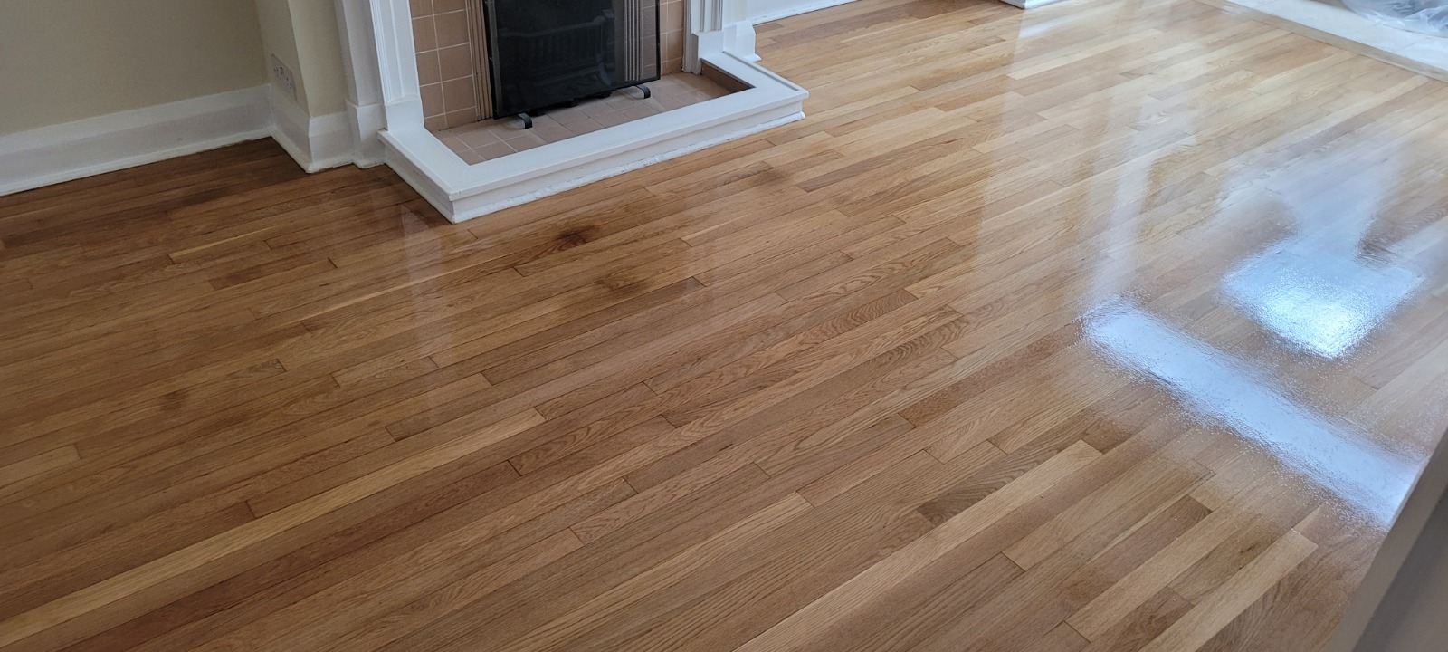 Furious Fixes in Woking: solid oak strip hardwood floor newly finished to a high-gloss sheen, reflections visible around the fireplace.