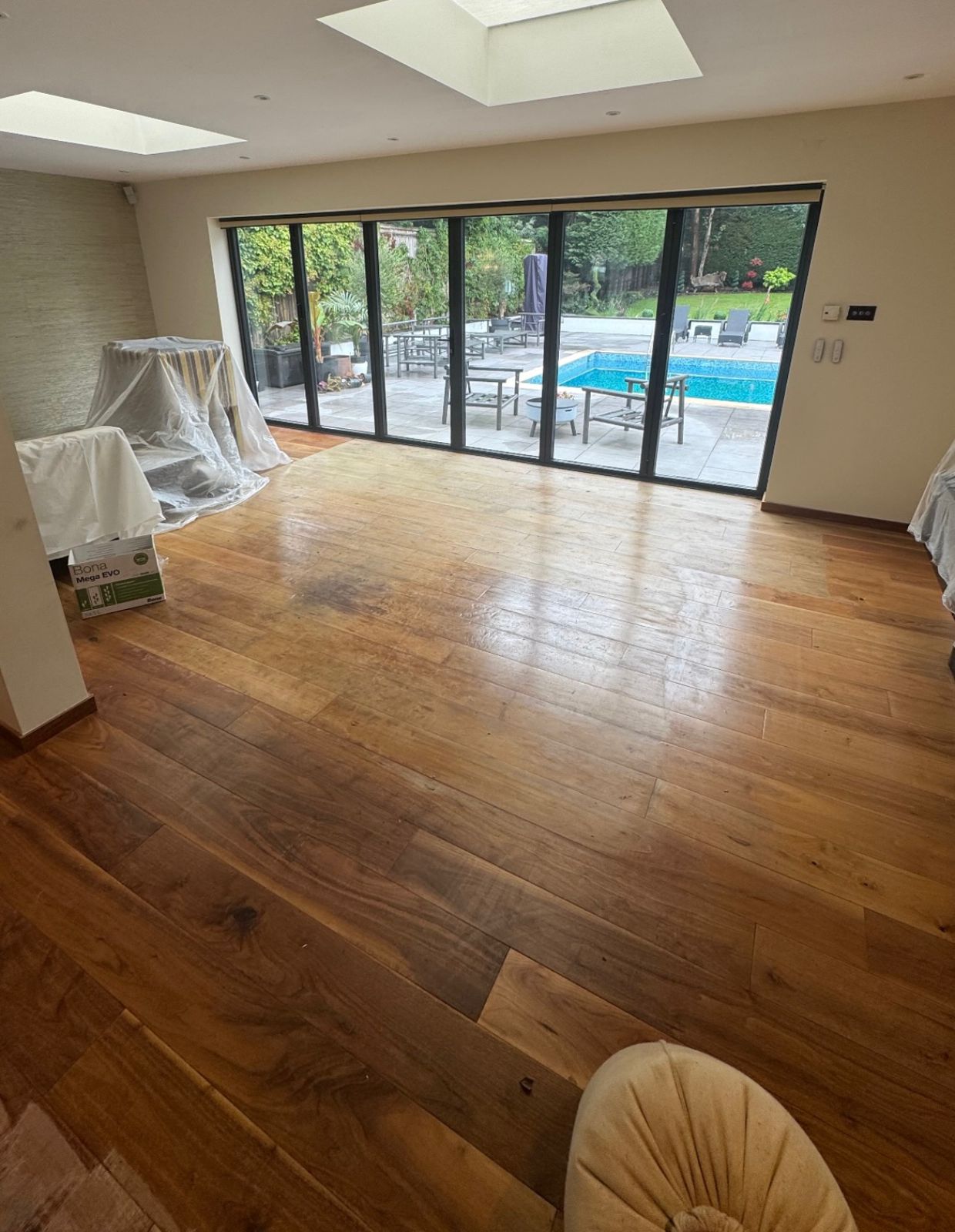 Furious Fixes in Woking: living room with solid walnut hardwood plank floor showing sun-fade and traffic wear near the bi-fold doors, before restoration.