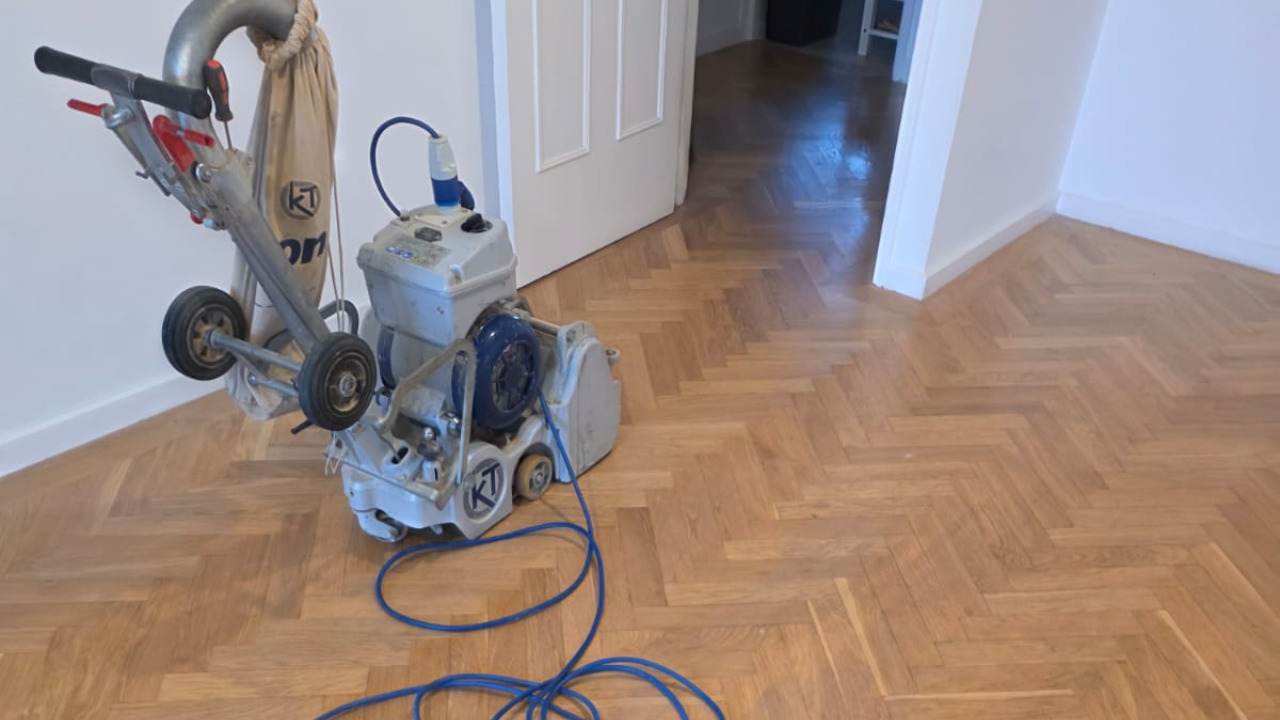 Wood Floor Sanding in Woking on an oak herringbone parquet floor, with a professional sanding machine positioned on the freshly sanded surface in a bright living area.