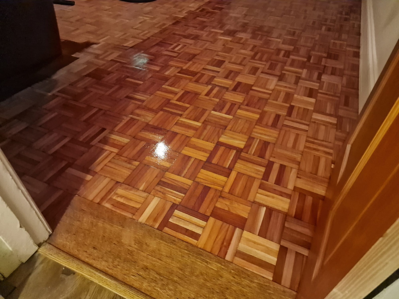 Wood Floor Sanding in Woking – freshly restored oak mosaic parquet hallway floor with a glossy finish seen through an open doorway.