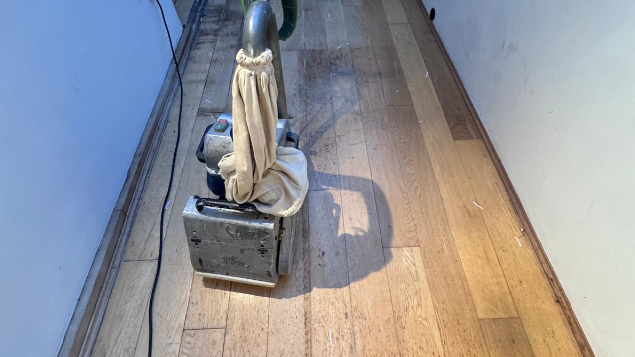 Wood Floor Sanding in Woking on an oak plank hardwood hallway floor, with a professional sanding machine removing dirt and scratches from the boards.